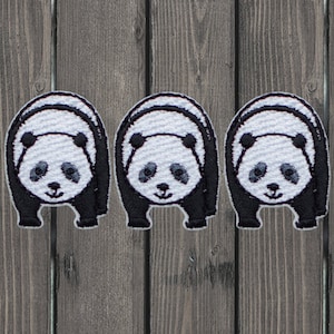May include: Three black and white panda bear embroidered patches. The patches are on a wood background.