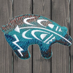 May include: A turquoise blue embroidered patch with a white bear design. The bear is stylized with geometric shapes and lines. The patch has a brown and blue ombre effect.