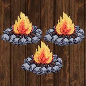 Könnte beinhalten: Drei gestickte Bügelbilder, die ein Lagerfeuer mit Flammen und Steinen darstellen. Die Patches sind hellgrau mit orangefarbenen und gelben Flammen.