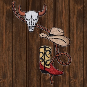 Puede incluir: Una bota vaquera de cuero marrón con un patrón amarillo y negro, un sombrero vaquero marrón y una calavera de vaca blanca con cuernos marrones, todo unido a una cuerda marrón.