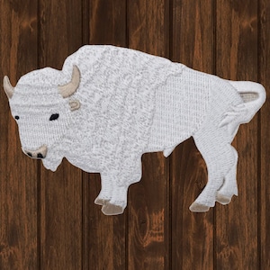 Peut inclure: Patch brodé blanc représentant un bison, avec des accents marrons pour les cornes et les sabots. Le patch est sur un fond en bois.