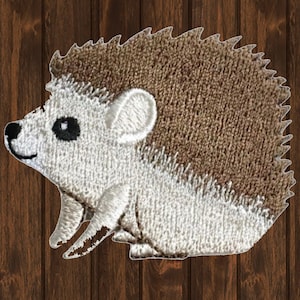 May include: Embroidered patch featuring a detailed hedgehog design. The hedgehog has a brown back, white belly, and a smiling face with black eyes. The patch is likely for clothing or accessories.