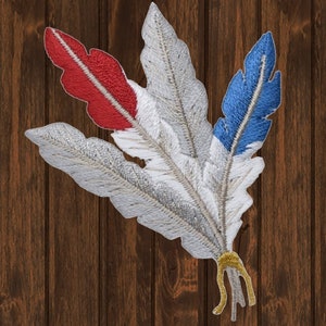 May include: Embroidered patch featuring three stylized feathers in red, white, and blue. The feathers have detailed stitching and a metallic silver outline. The base of the feathers is tied with gold thread, creating a decorative emblem.