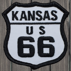 May include: White patch with black embroidered text and numbers. The text reads "KANSAS US 66".
