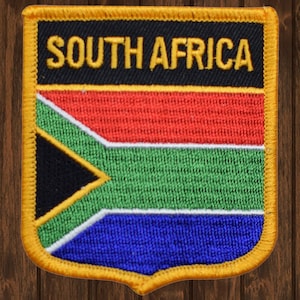 May include: A yellow embroidered patch with a shield shape. The patch features the South African flag with red, white, black, green, and blue colors. The text "SOUTH AFRICA" is embroidered in yellow on a black background.