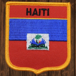 May include: A red, blue, and green embroidered patch with the word "HAITI" in black lettering. The patch is surrounded by a yellow border and has a shield shape.