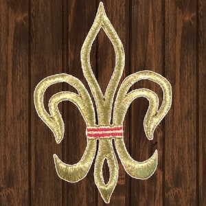 May include: A gold-colored fleur-de-lis with a red and white striped band across the center.