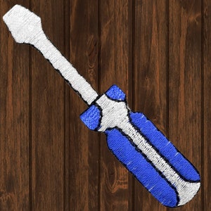 以下が含まれることがあります： 青と白の刺繍されたドライバーのパッチ。ドライバーは茶色の木製の背景の上にあります。