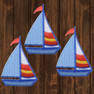 May include: Three blue and white sailboat patches with red accents. The sailboats are embroidered and have a simple design.
