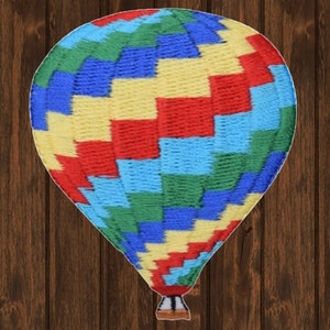 Pode incluir: Um balão de ar quente colorido com um padrão geométrico vermelho, amarelo, azul e verde. O balão é feito de tecido e tem uma cesta na parte inferior.