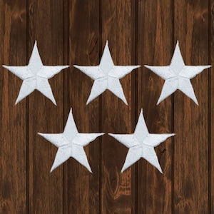 May include: Five white felt star-shaped patches on a brown wooden background.