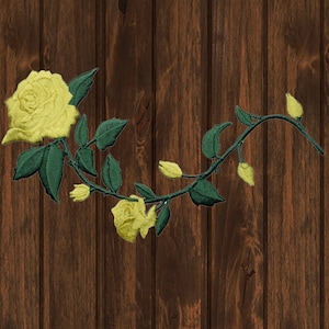 May include: A yellow rose with green leaves and stems on a brown wooden background.