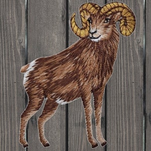 May include: Embroidered patch of a brown bighorn sheep with large curled horns. The sheep is standing on a wood background.