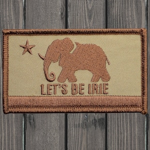 Peut inclure: Un patch brodé beige et marron avec une silhouette d'éléphant marron et une étoile. Le texte "LET'S BE IRIE" est brodé sous l'éléphant.