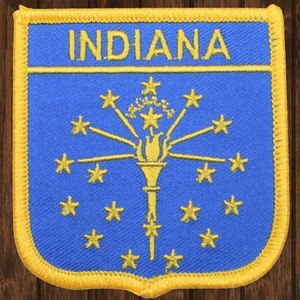 May include: A blue and gold embroidered patch with the word "INDIANA" at the top and the state seal of Indiana in the center. The seal features a torch with 13 stars surrounding it.