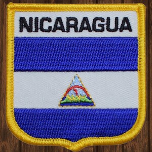 May include: Embroidered patch with a blue, white, and blue Nicaraguan flag. The flag features a triangle with a red border and a white star in the center. The words "NICARAGUA" are embroidered in black at the top of the patch.