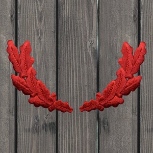 May include: Two red fabric oak leaf wreaths on a wooden background.