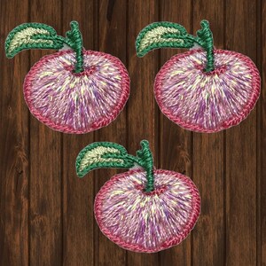 May include: Three pink embroidered felt apple patches with green stems and leaves. The apples have a white and purple swirl design.