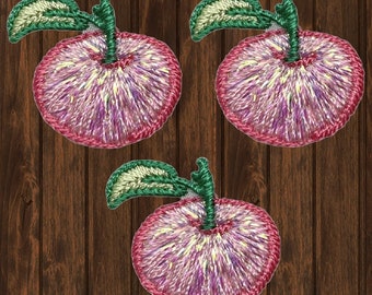 Puede incluir: Tres parches de manzana de fieltro bordados en rosa con tallos y hojas verdes. Las manzanas tienen un diseño de remolino blanco y morado.