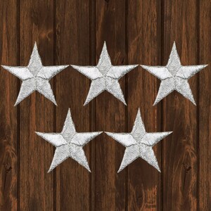 Pode incluir: Seis estrelas bordadas prateadas sobre um fundo de madeira castanho.