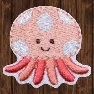 May include: A pink embroidered octopus with a smiling face and white iridescent spots. The octopus has eight pink tentacles.