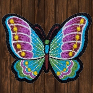 May include: A colorful embroidered butterfly patch with pink, blue, green, and yellow accents. The butterfly is outlined in black and has a detailed design.