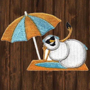 May include: Embroidered patch of a white bird with a blue and orange umbrella on a beach. The bird is sitting on a blue and orange towel.