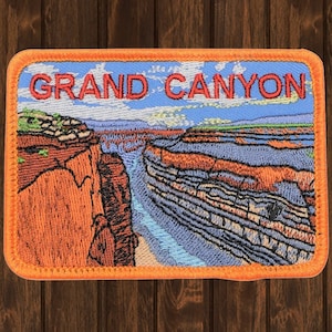 May include: Embroidered patch with an orange border featuring a scenic view of the Grand Canyon with the text "GRAND CANYON" in red.