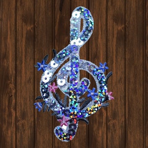 May include: A silver and blue sequined treble clef with floral accents. The treble clef is a musical symbol.