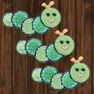 Op de afbeelding: Drie groene geborduurde rupsenpatches met gele antennes en glimlachende gezichten. De rupsen zijn gemaakt van vilt en hebben een gestikte omtrek.