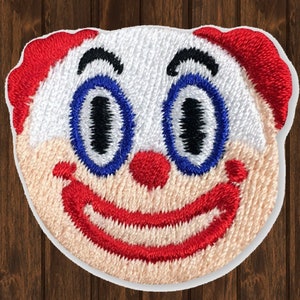 Può includere: Toppa ricamata con un viso di clown sorridente con capelli rossi, occhi blu e un sorriso rosso. Il viso del clown è bianco con un incarnato rosa chiaro.