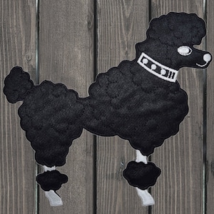 May include: Black felt poodle applique with white felt details. The poodle has a white collar with black stitching and a white eye.