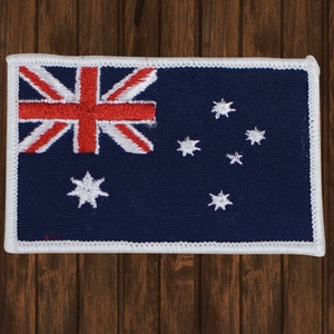 Op de afbeelding: Een wit omrande patch met de Australische vlag. De vlag is blauw met een rood, wit en blauw Union Jack in de linkerbovenhoek en een sterrenbeeld van zeven witte sterren in de rechterbenedenhoek.