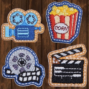 May include: Four embroidered patches with a movie theme. A blue and gold film camera, a silver film reel, a black and white clapperboard, and a red and white box of popcorn with the word "corn" on it.