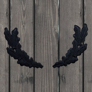 May include: Two black fabric oak leaf wreaths on a wood background.