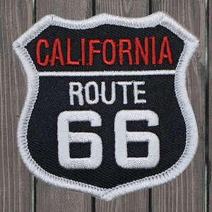 Puede incluir: Un parche bordado en blanco y negro con un borde blanco. El parche presenta el texto "CALIFORNIA ROUTE 66" en letras blancas y rojas.