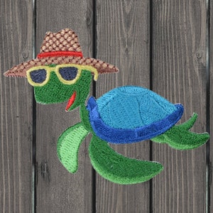 Puede incluir: Una tortuga verde que lleva un sombrero de paja marrón y blanco con una banda roja y gafas de sol. La tortuga tiene un caparazón azul y está bordada sobre un fondo de madera.