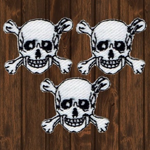 May include: Three white skull and crossbones patches. The skulls are embroidered with black thread and have a white background. The crossbones are also embroidered with black thread.