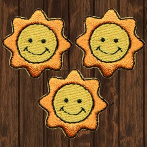 May include: Three yellow embroidered iron-on patches shaped like suns with smiling faces. The suns have orange outlines.