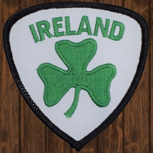 May include: White embroidered patch with a green shamrock and the word "IRELAND" in black lettering. The patch has a black border and a rounded triangular shape.