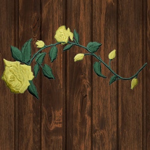 May include: A yellow rose with green leaves and stem on a brown wooden background.