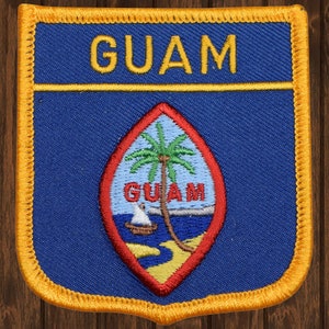 May include: A blue and red embroidered patch with the word "GUAM" in yellow lettering and a seal with a palm tree and the word "GUAM" in white lettering.