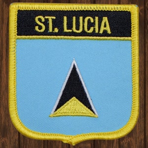 May include: A yellow, black, and white embroidered patch with the text "ST. LUCIA" in yellow letters on a black background. The patch features the flag of Saint Lucia, a blue background with a yellow, black, and white triangle.