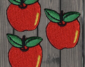 Puede incluir: Tres parches de manzana de fieltro rojo con hojas de fieltro verde. Las manzanas tienen un contorno amarillo.