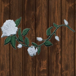 May include: White embroidered rose vine with green leaves on a brown wooden background.