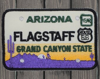 Puede incluir: Parche bordado blanco y amarillo con el texto "Arizona", "Flagstaff", "Grand Canyon State" y "Ruta 66". El parche presenta una cordillera púrpura con un cactus y un saguaro.
