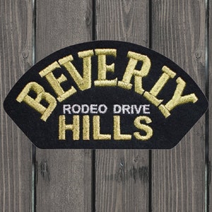 Könnte beinhalten: Ein schwarzer Filz-Patch mit goldfarbener Stickerei, auf dem "Beverly Rodeo Drive Hills" steht.