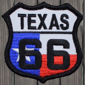 Può includere: Toppa ricamata a forma di scudo, con la scritta "TEXAS" in lettere nere sopra il numero "66". La toppa incorpora i colori della bandiera dello stato del Texas: blu, bianco e rosso, con un bordo nero.