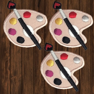 May include: Three iron-on patches featuring a paint palette and paintbrush. The palette is beige with five paint wells in various colours, including red, yellow, purple, black, and white. The paintbrush is black with a red handle.