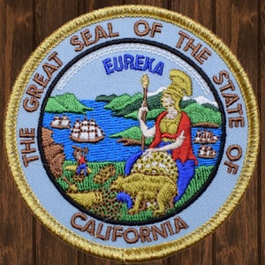 May include: A blue and gold embroidered patch featuring the Great Seal of the State of California. The seal depicts a woman holding a staff, a bear, and a scene of a bay with ships. The text "The Great Seal of the State of California" and "Eureka" are visible.
